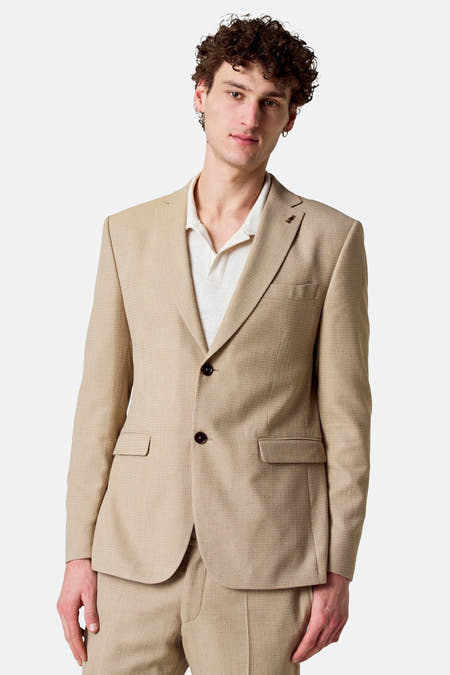 Blazer beige de Le Fabuleux Marcel de Bruxelles, avec deux boutons, col revers et porté sur un polo blanc.