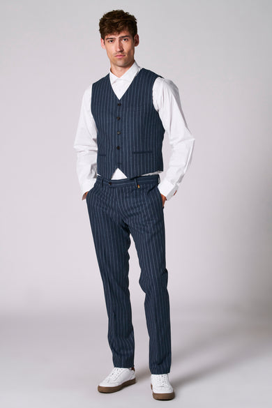Gilet bleu de Le Fabuleux Marcel de Bruxelles, porté avec un chemisier blanc et un pantalon à rayures coordonnés.