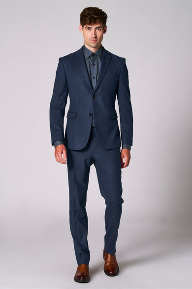 Blazer bleu de Le Fabuleux Marcel de Bruxelles, porté avec un chemisier à carreaux et des chaussures marrons.