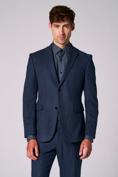 Blazer bleu de Le Fabuleux Marcel de Bruxelles, avec col revers et motif subtil de carreaux sur la chemise en dessous.