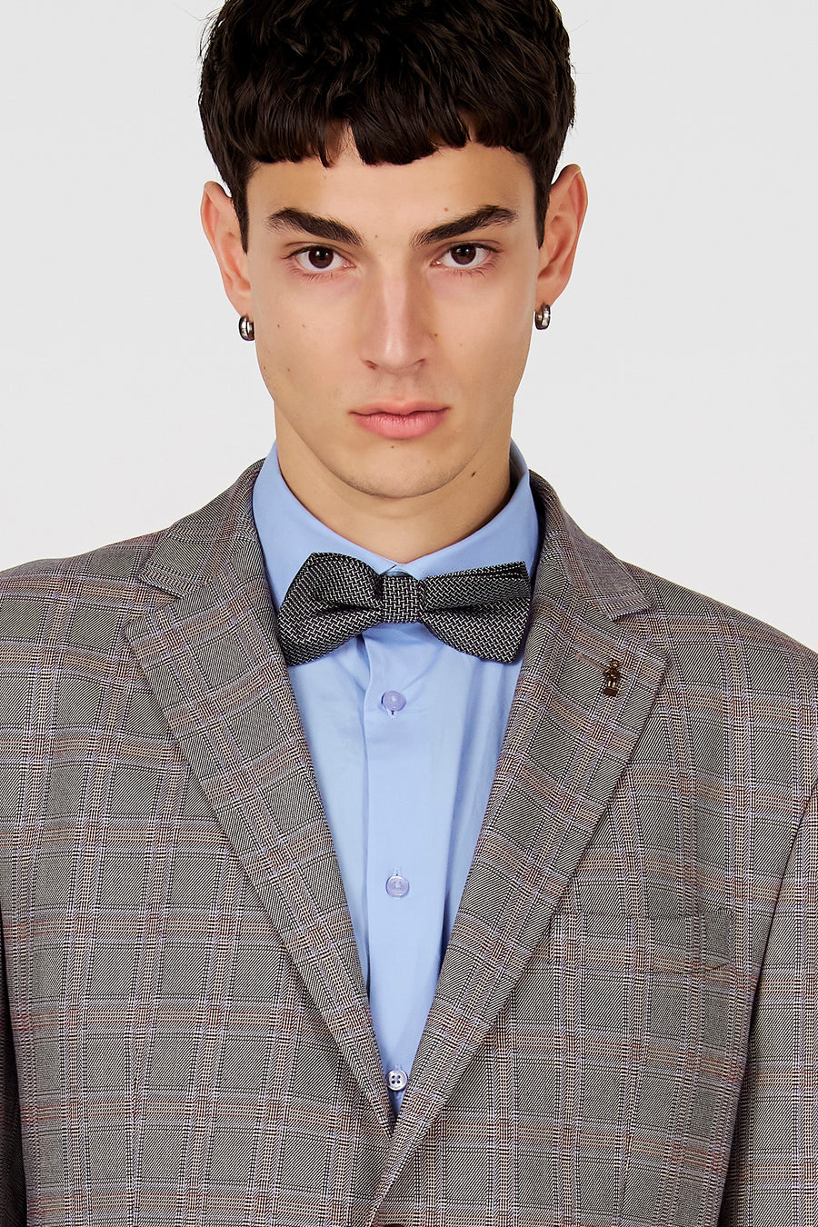 Blazer marron de Le Fabuleux Marcel de Bruxelles, à motif à carreaux, porté sur une chemise bleu clair avec un nœud papillon noir.