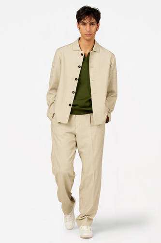 Blazer beige de Le Fabuleux Marcel de Bruxelles, avec boutons foncés, combiné avec un pull vert et un pantalon assorti.