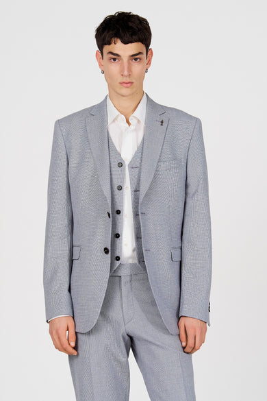 Blauwe blazer van Le Fabuleux Marcel de Bruxelles, met een fijn ruitpatroon, gedragen over een wit overhemd en gilet.
