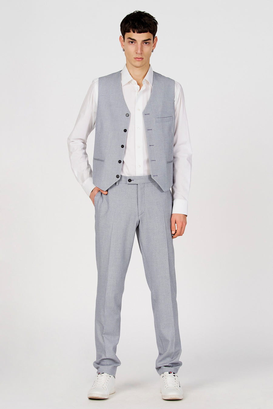 Gilet bleu de Le Fabuleux Marcel de Bruxelles, avec boutons noirs, combiné avec une chemise blanche et un pantalon gris.
