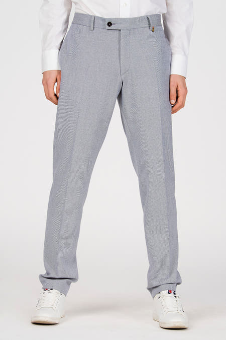 Blauwe kostuumbroek van Le Fabuleux Marcel de Bruxelles, met een subtiel patroon en een enkele knoopsluiting, gedragen met een wit overhemd en witte sneakers.
