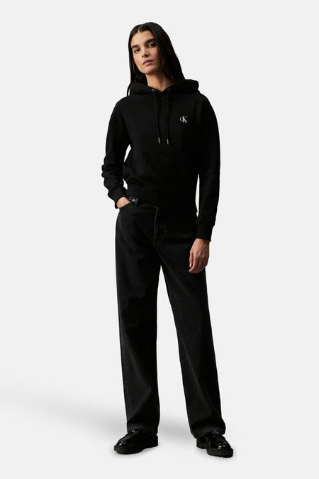 Pull-over noir avec capuche de Calvin Klein, porté avec des jeans noirs larges et des chaussures noires.