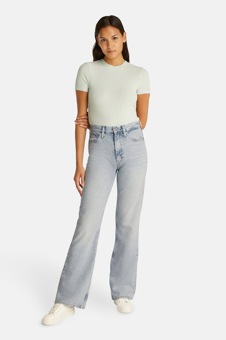 Jeans bootcut van lichtblauw denim van Calvin Klein, gedragen met een shirt met structuur en witte sneakers.
