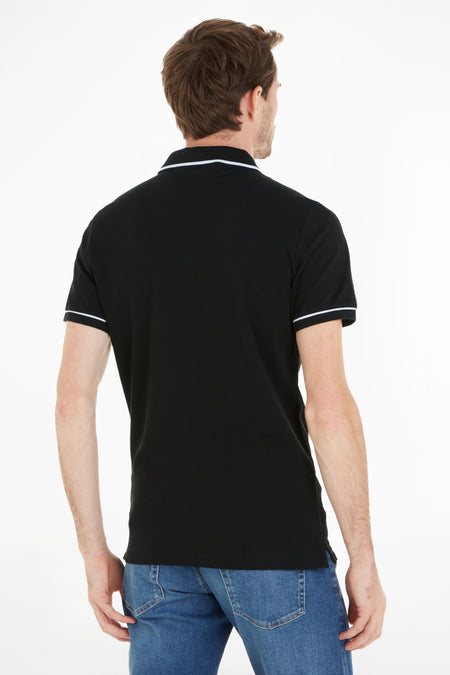 Zwarte polo van Calvin Klein met witte accenten op de kraag en mouwen, gedragen met een blauwe jeans, rugaanzicht.
