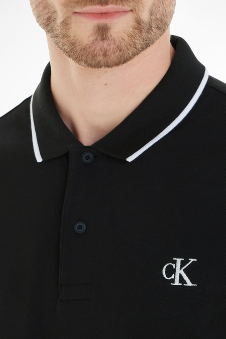 Zwarte polo van Calvin Klein, met korte mouwen en een wit afgebiesde kraag, met ck-logo op de borst.
