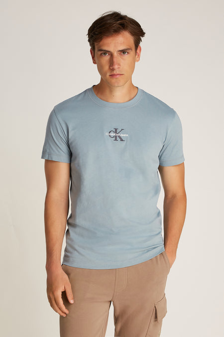 T-shirt bleu clair à manches courtes de Calvin Klein Jeans, avec un petit logo sur la poitrine et porté avec des shorts kaki.