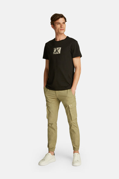 T-shirt noir à manches courtes de Calvin Klein, vu porté en arrière avec un pantalon kaki.