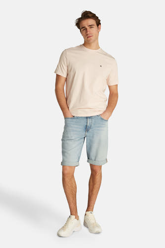 Jeansshort in lichtblauw denim van Calvin Klein, met omgeslagen pijpen en gedragen met een T-shirt en witte sneakers.
