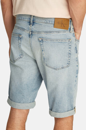Jean court en denim bleu clair de Calvin Klein, avec un zip suré et une étiquette en cuir brun à l'arrière.
