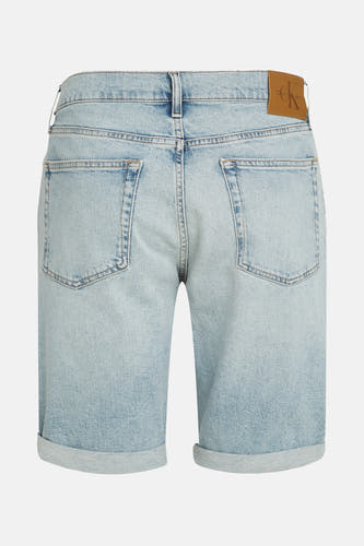 Jean court en denim bleu clair de Calvin Klein, avec des poches rabattues et une étiquette en cuir marron sur la ceinture.