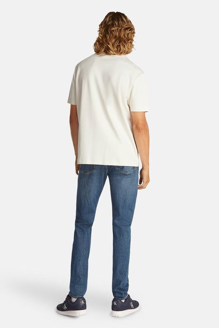 T-shirt écru à manches courtes de Calvin Klein, dos, associé à des jeans bleus et des chaussures bleu marine avec logo.