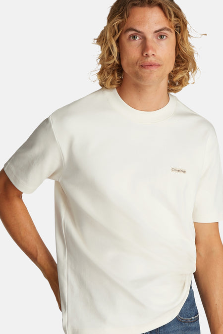 T-shirt écru à manches courtes de Calvin Klein, design simple, porté avec un jean bleu.