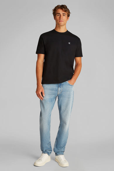 T-shirt noir à manches courtes de Calvin Klein, porté avec un jeans bleu et des baskets blanches.