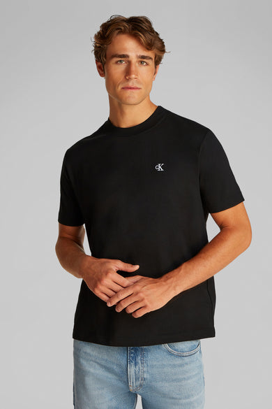 T-shirt noir à manches courtes de Calvin Klein, avec un petit logo sur la poitrine, porté avec un jean bleu.