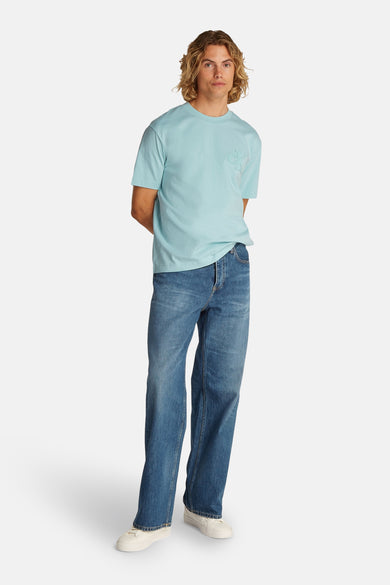Turquoise T-shirt met korte mouwen van Calvin Klein, gedragen met wijde jeans en witte sneakers.

