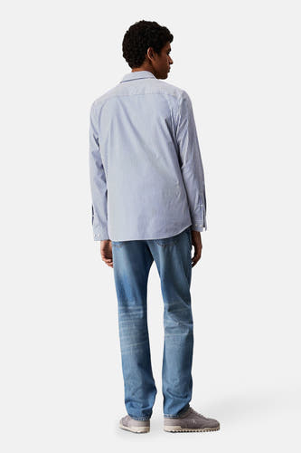 Jeanon bleu denim Calvin Klein, avec un chemisier à rayures et des chaussures grises.