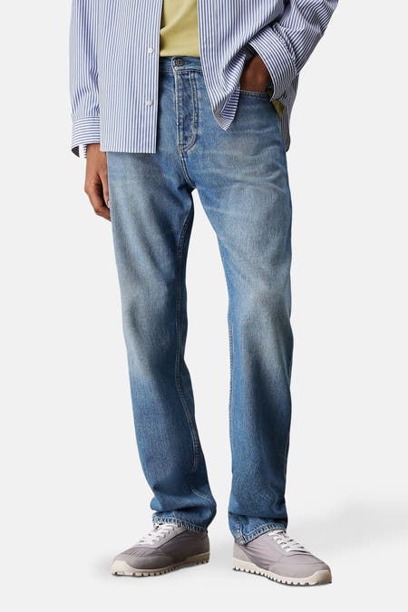 Jeans straight mid blue denim van Calvin Klein, met een licht verwassen effect en grijze sneakers.
