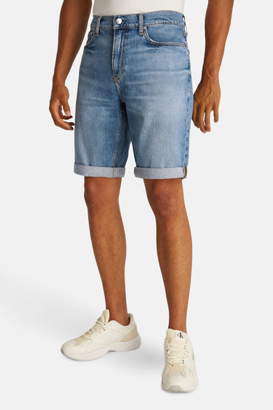Jeansshort in lichtblauw denim van Calvin Klein, met opgerolde pijpen en gedragen met crèmekleurige sneakers.
