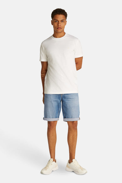 Jeansshort van lichtblauw denim van Calvin Klein, met opgerolde pijpen en gecombineerd met een wit T-shirt en crèmekleurige sneakers.

