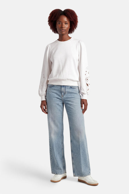 Witte sweater van HAILYS, met lange mouwen met bloemendetails, gecombineerd met wijde jeans en witte sneakers.
