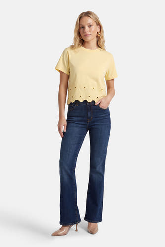 Geel T-shirt met korte mouwen van HAILYS, afgewerkt met broderie langs de zoom, gecombineerd met donkerblauwe jeans en nude hakken.
