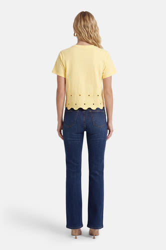 T-shirt à manches courtes jaune de HAILYS, avec un ourlet en dentelle et porté avec un jean bleu foncé et des talons.