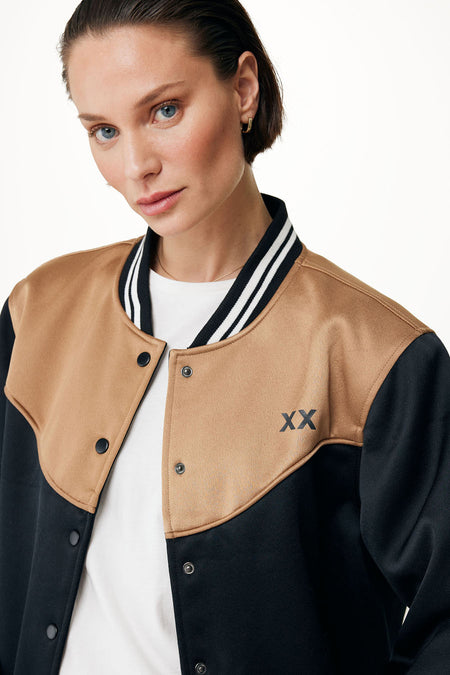 Zwarte korte jas van MEXX, met karamelkleurige accenten en de letters XX, gedragen over een wit shirt.