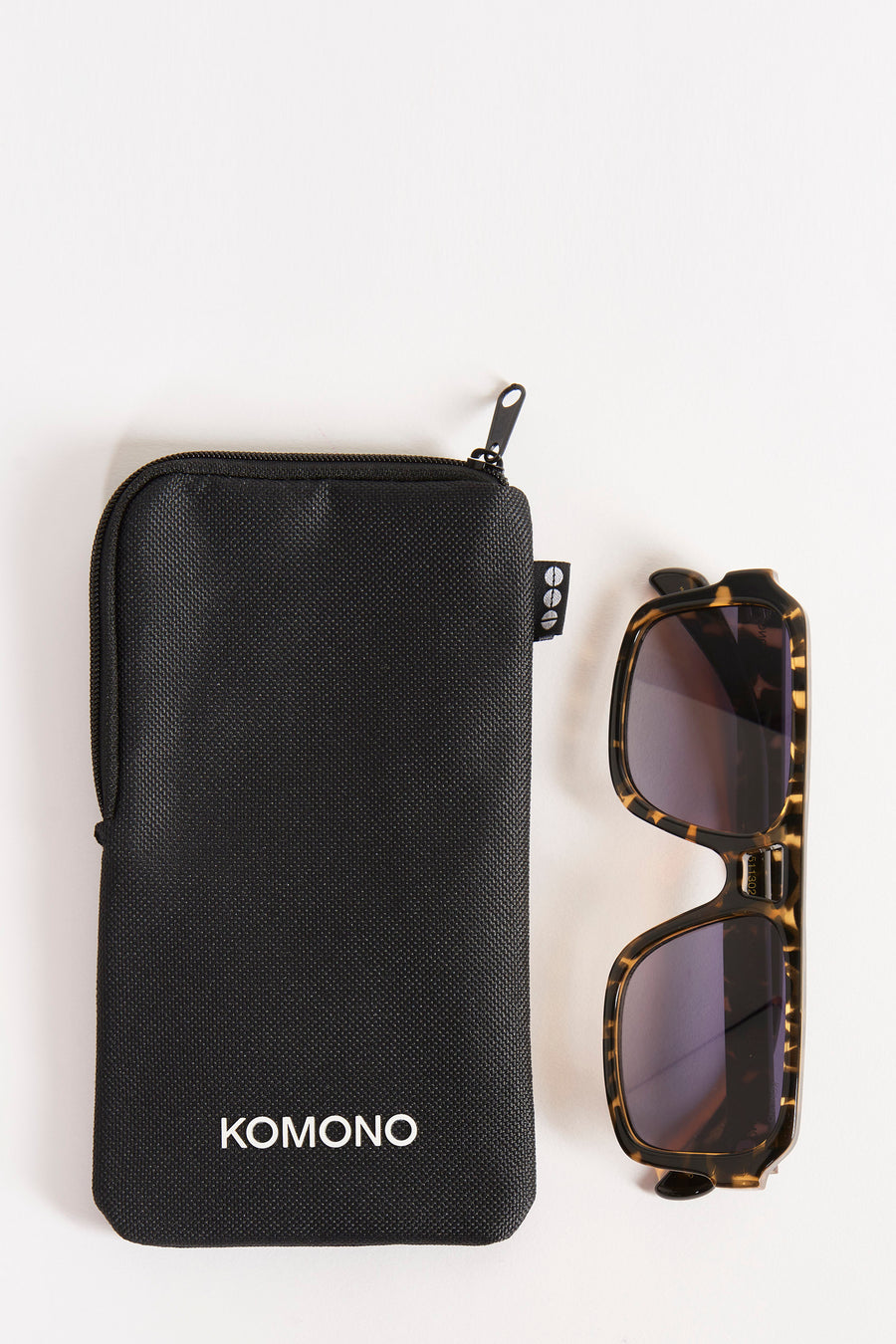 Groene bril van KOMONO, naast een zwarte beschermhoes met het merklogo.