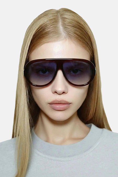 Bordeauxrode zonnebril van KOMONO met donkere glazen, gedragen door een model met blond haar en een lichtgrijze trui.