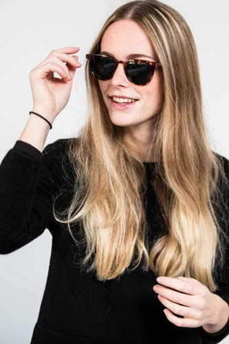 Groene zonnebril van KOMONO, gedragen door een vrouw met lang blond haar en een zwarte trui.
