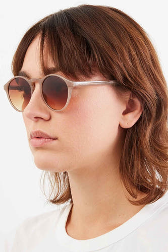 Beige zonnebril van KOMONO, met een bruin-gele gradiënt lens en gedragen door een vrouw in een wit shirt.
