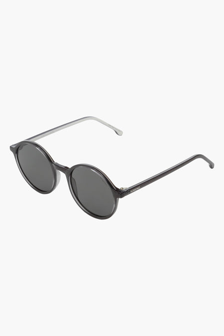Lunettes de soleil grises de KOMONO, avec des verres ovales et des branches fines couleur argent.