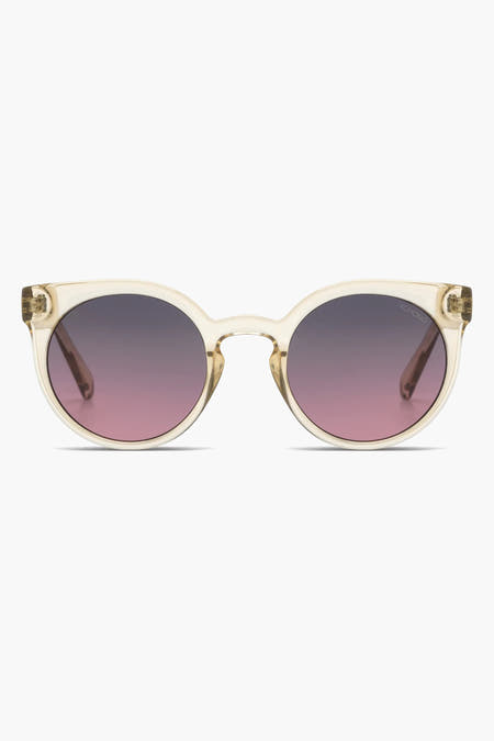 Lunettes de soleil beige de Komono avec des verres teintés violet-rose et un cadre transparent.