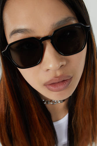 Zwarte zonnebril van KOMONO, close-up van het gezicht van een model met een zilveren ketting.
