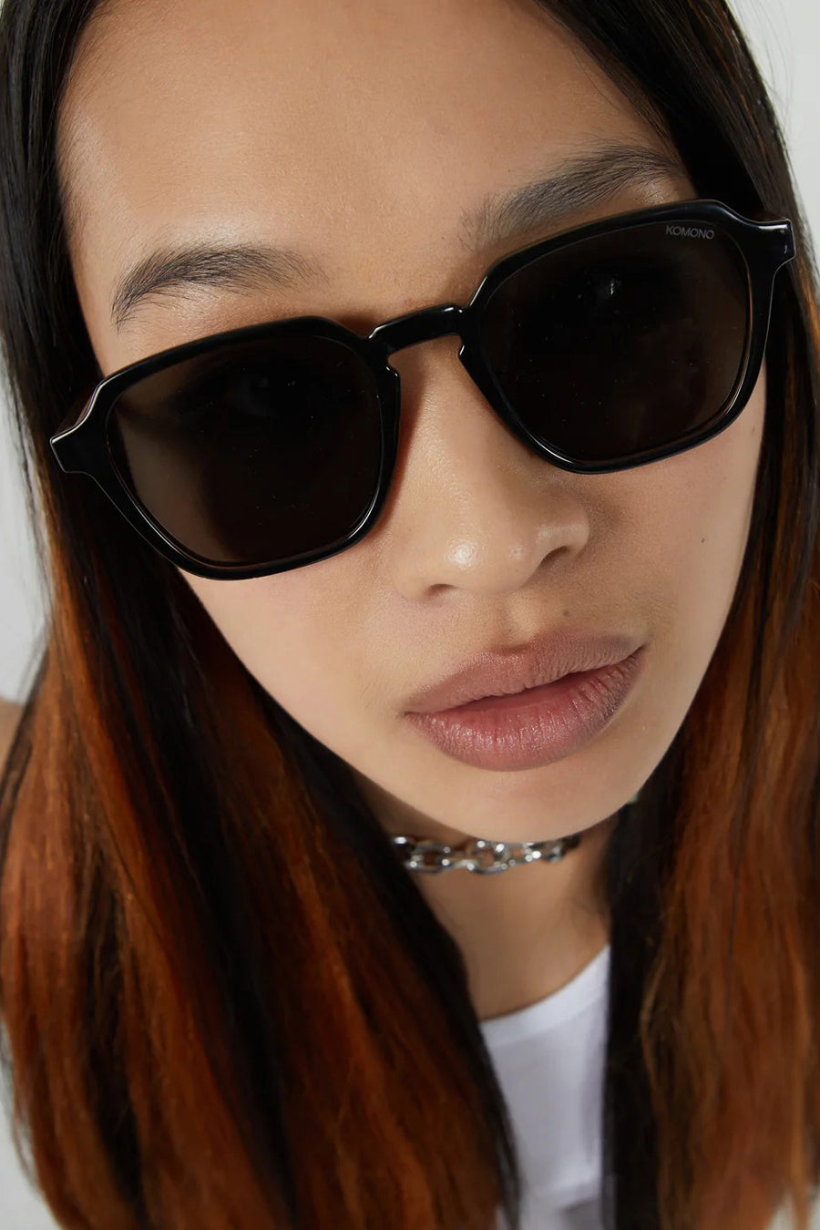 Zwarte zonnebril van KOMONO, gedragen met zilverkleurige halsketting en wit shirt.