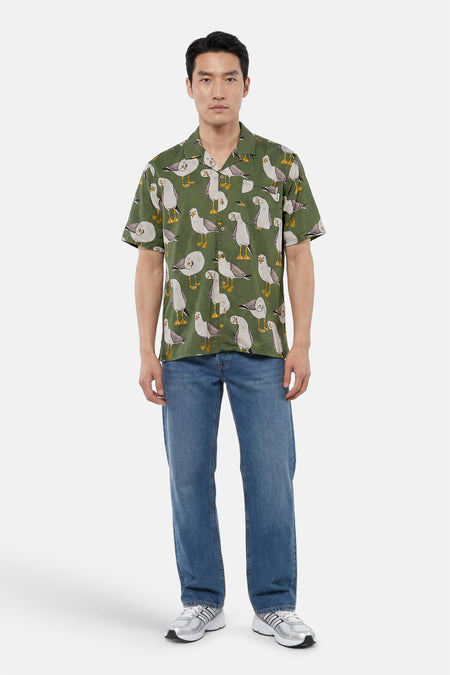 Groen hemd met korte mouwen van LAKOR met meeuwenprint, gedragen door een man met blauwe jeans en zilveren sneakers.