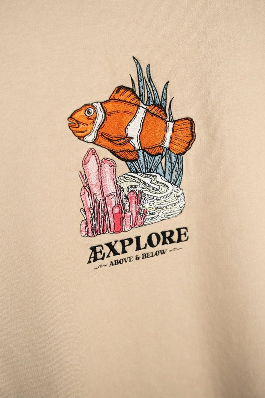 Ecru sweater met ronde hals van LAKOR, met een geborduurde afbeelding van een clownvis en de tekst "EXPLORE".

