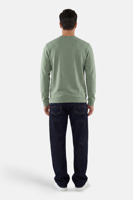 Groene sweater van LAKOR, achterkant, gedragen met donkere spijkerbroek en witte sneakers.