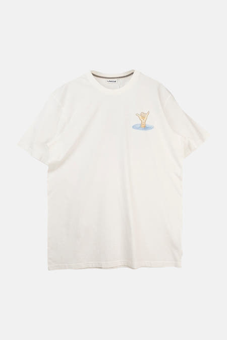Wit T-shirt van LAKOR, met een kleine illustratie van een hand die een shaka-teken maakt, omringd door water.

