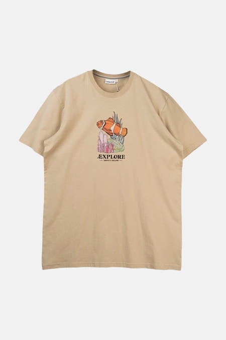 Beige T-shirt van LAKOR, met een afbeelding van een clownvis en de tekst "EXPLORE ABOVE & BELOW".