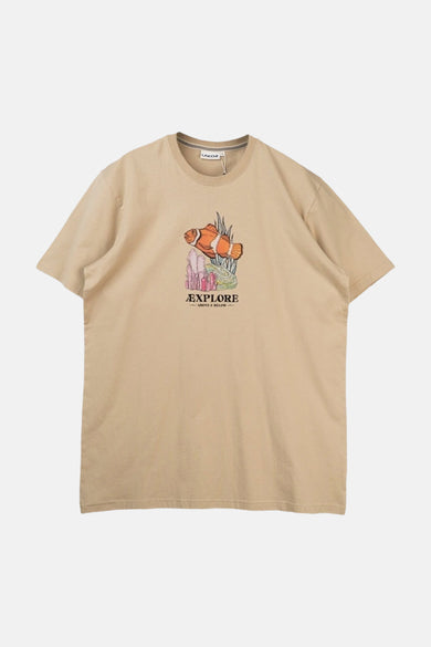 Beige T-shirt van LAKOR, met een afbeelding van een clownvis en de tekst "EXPLORE ABOVE & BELOW".