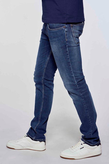 Slim jeans in mid blue denim van Lee Cooper®, getoond van opzij met witte sneakers en donkerblauw shirt