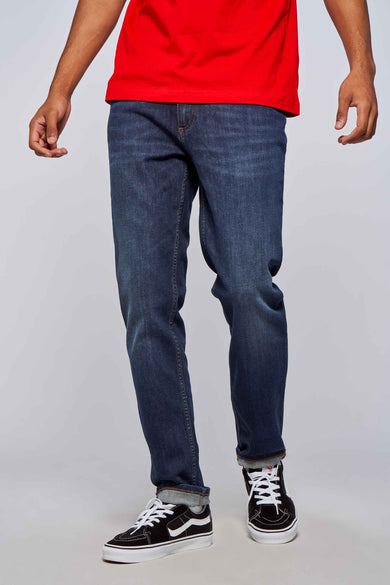 Donkerblauwe rechte jeans van Lee Cooper, gedragen met zwarte en witte sneakers, op een lichte achtergrond.
