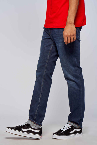 Donkerblauwe rechte jeans van Lee Cooper, met zichtbare omslag en sneakers met streep.