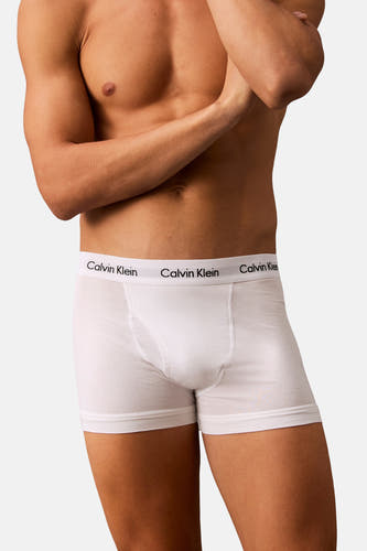 Slip blanc de Calvin Klein, avec une bande élastique à logo, porté par un homme les les bras croisés.