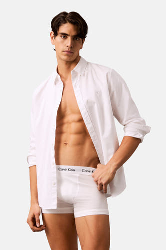 Robe blanche de Calvin Klein, portée avec un chemisier blanc ouvert, contre un fond neutre.